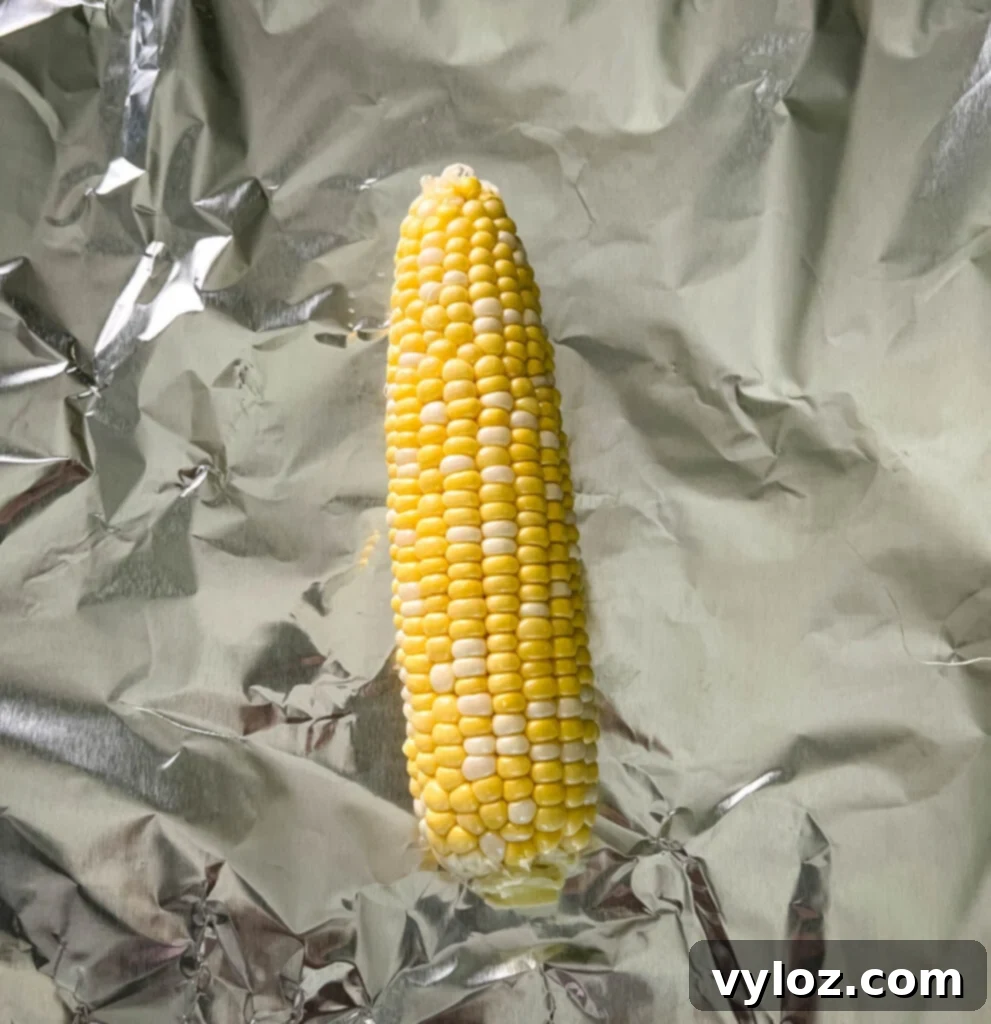 An ear of corn on foil, drizzled with seasoning, before wrapping