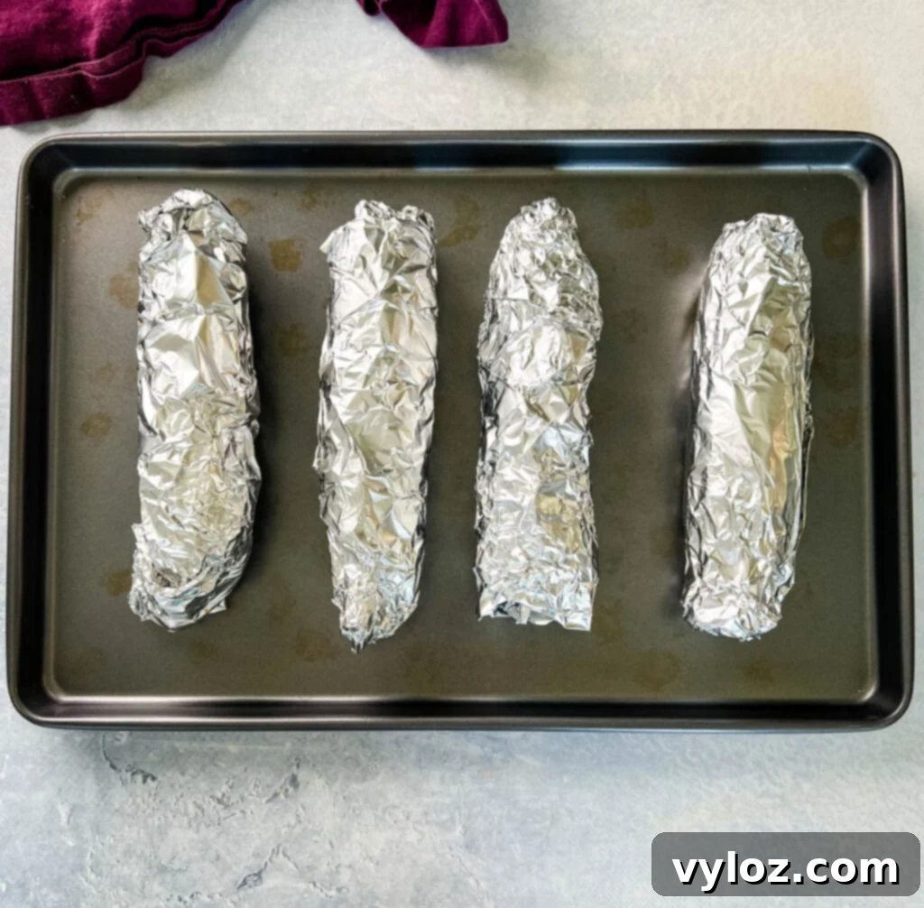 Baked oven roasted corn on the cob wrapped in foil on a baking sheet