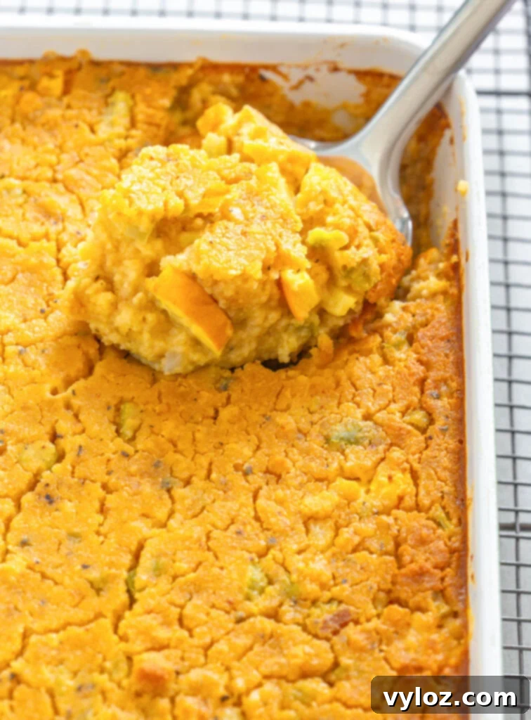 A close-up shot of a spoonful of unbaked squash dressing in a baking dish, highlighting its rich, moist texture before cooking.