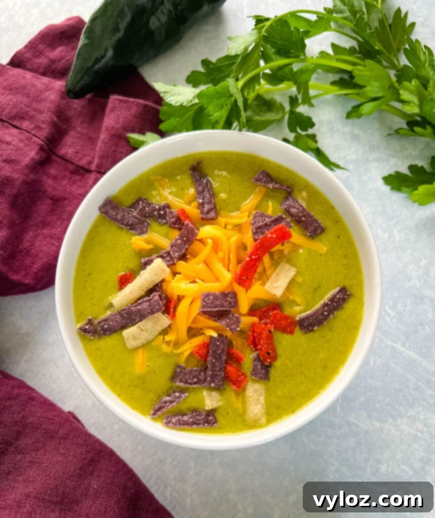 roasted creamy poblano pepper soup in a white bowl with shredded cheese and tortilla strips