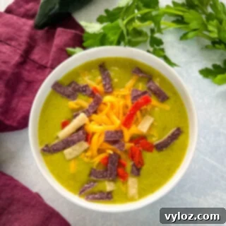 roasted creamy poblano pepper soup in a white bowl with shredded cheese and tortilla strips