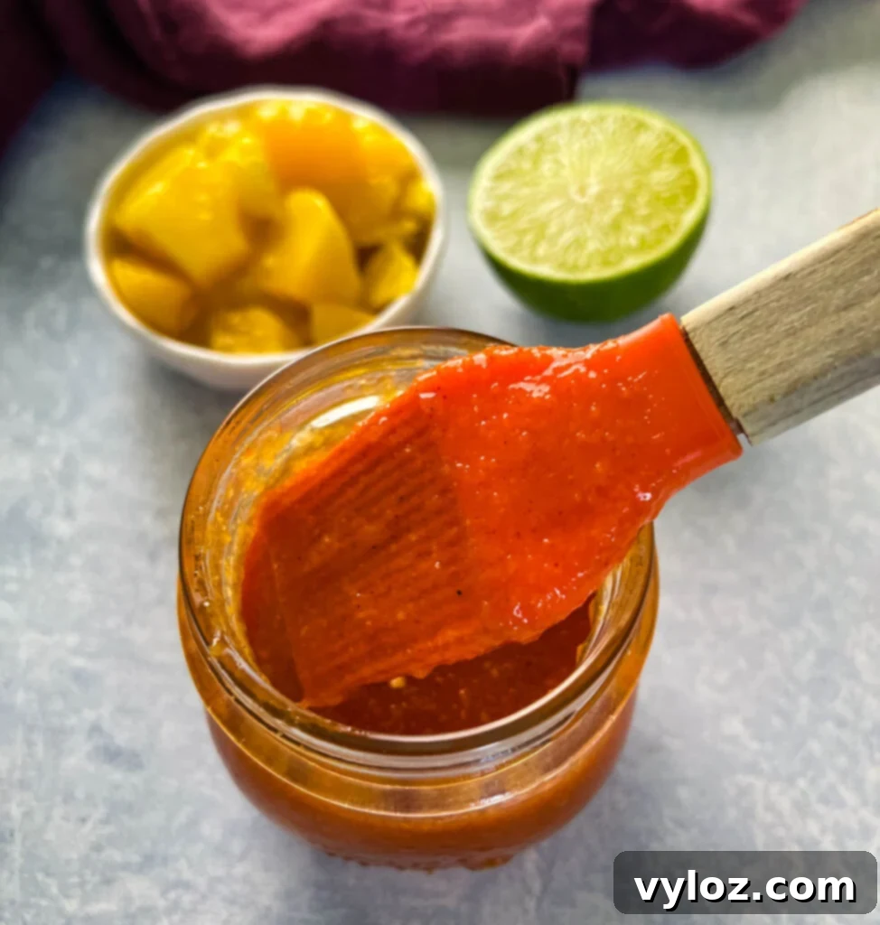 A cooking brush applying vibrant mango habanero sauce to a dish, illustrating its perfect glazing consistency.