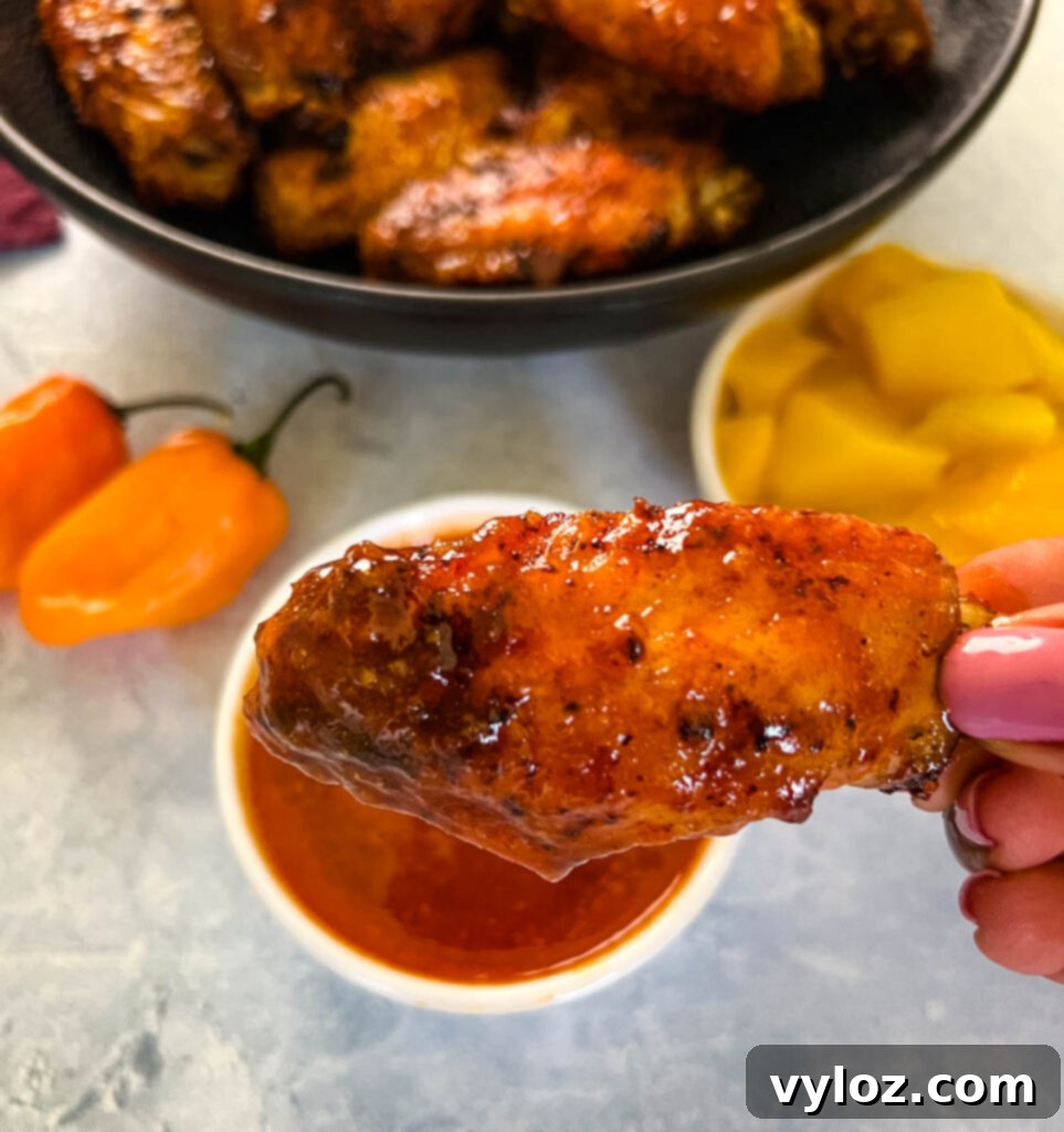 A person holding a mango habanero wing, dipped in extra sauce.