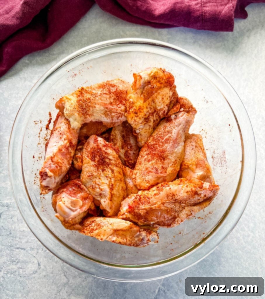 Raw chicken wings seasoned with spices in a glass bowl.