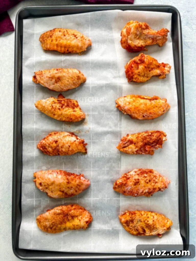 Seasoned chicken wings arranged on a baking sheet lined with parchment paper.