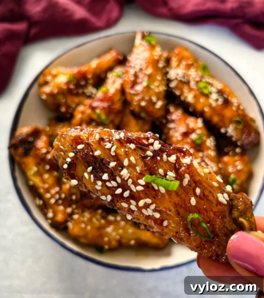 person holding teriyaki chicken wing with sesame seeds