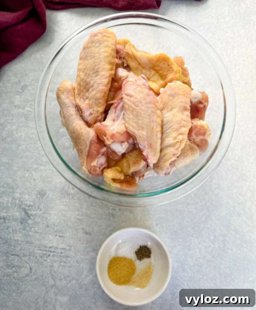 raw chicken wings in a glass bowl with a bowl of spices