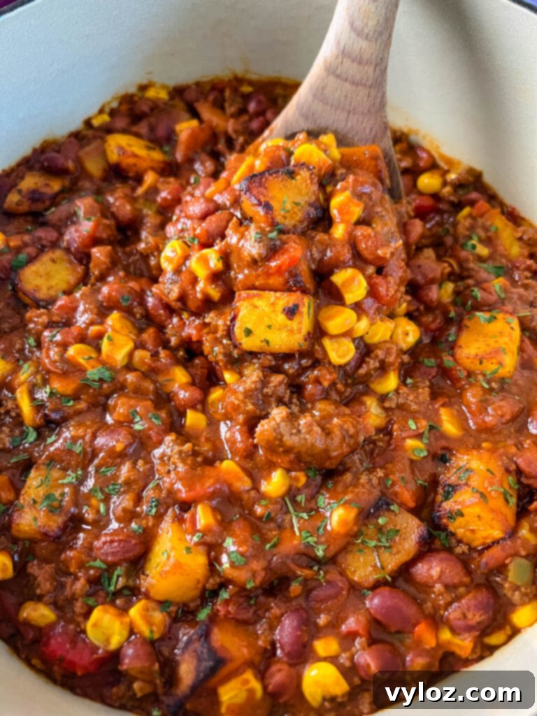 Hearty Butternut Squash Chili with Your Choice of Meat 2 A large wooden spoonful of vibrant butternut squash chili, garnished with fresh herbs.