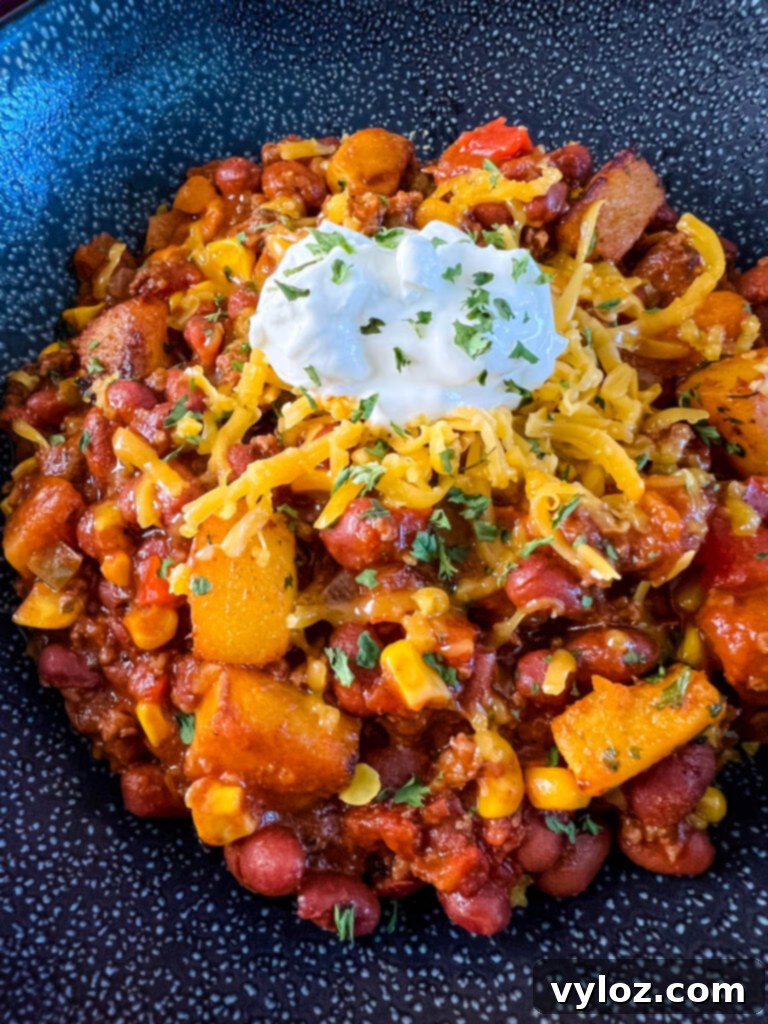 Hearty Butternut Squash Chili with Your Choice of Meat 12 Butternut squash chili served in a black bowl, garnished with a swirl of sour cream and fresh herbs.