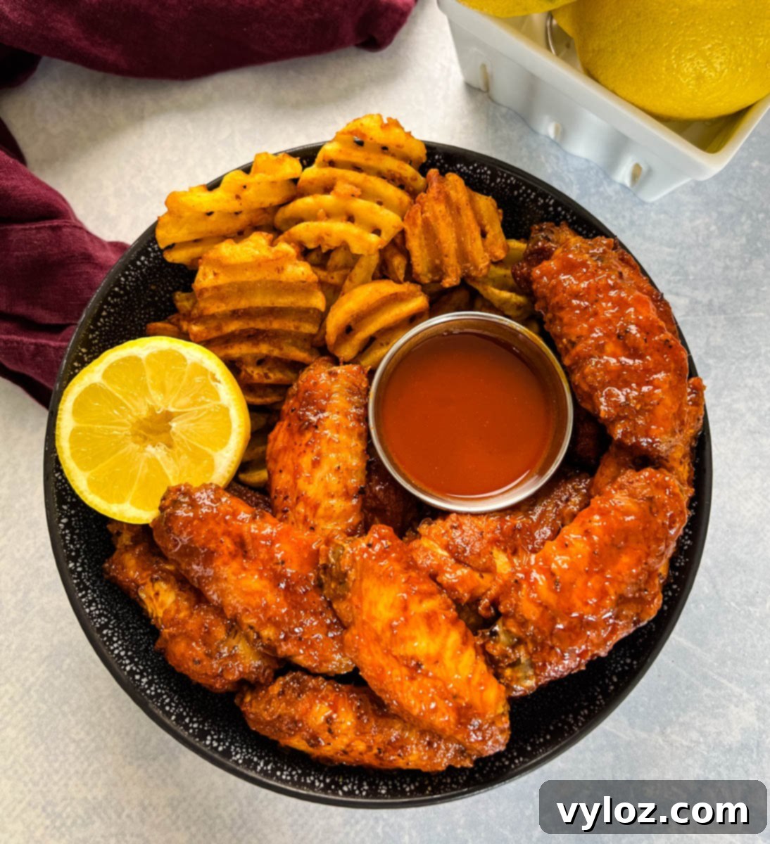 hot lemon pepper chicken wings in a black bowl with fresh lemon and hot sauce