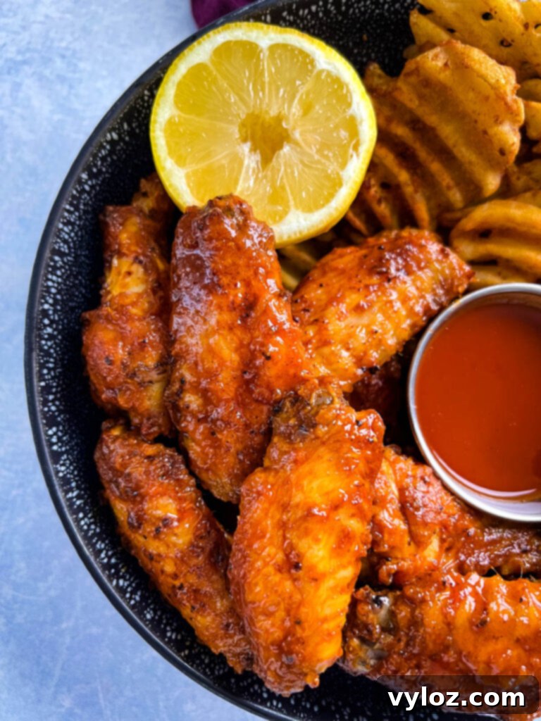 hot lemon pepper chicken wings in a black bowl with fresh lemon and hot sauce