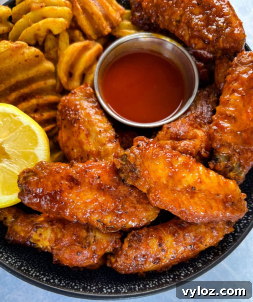 hot lemon pepper chicken wings in a black bowl with fresh lemon and hot sauce