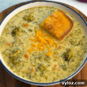 Creamy Slow Cooker Broccoli Cheddar Soup 9 Overhead view of a bowl filled with creamy broccoli cheddar soup, chunks of broccoli and carrots, a sprinkle of shredded cheddar, and a piece of cornbread resting in the soup.