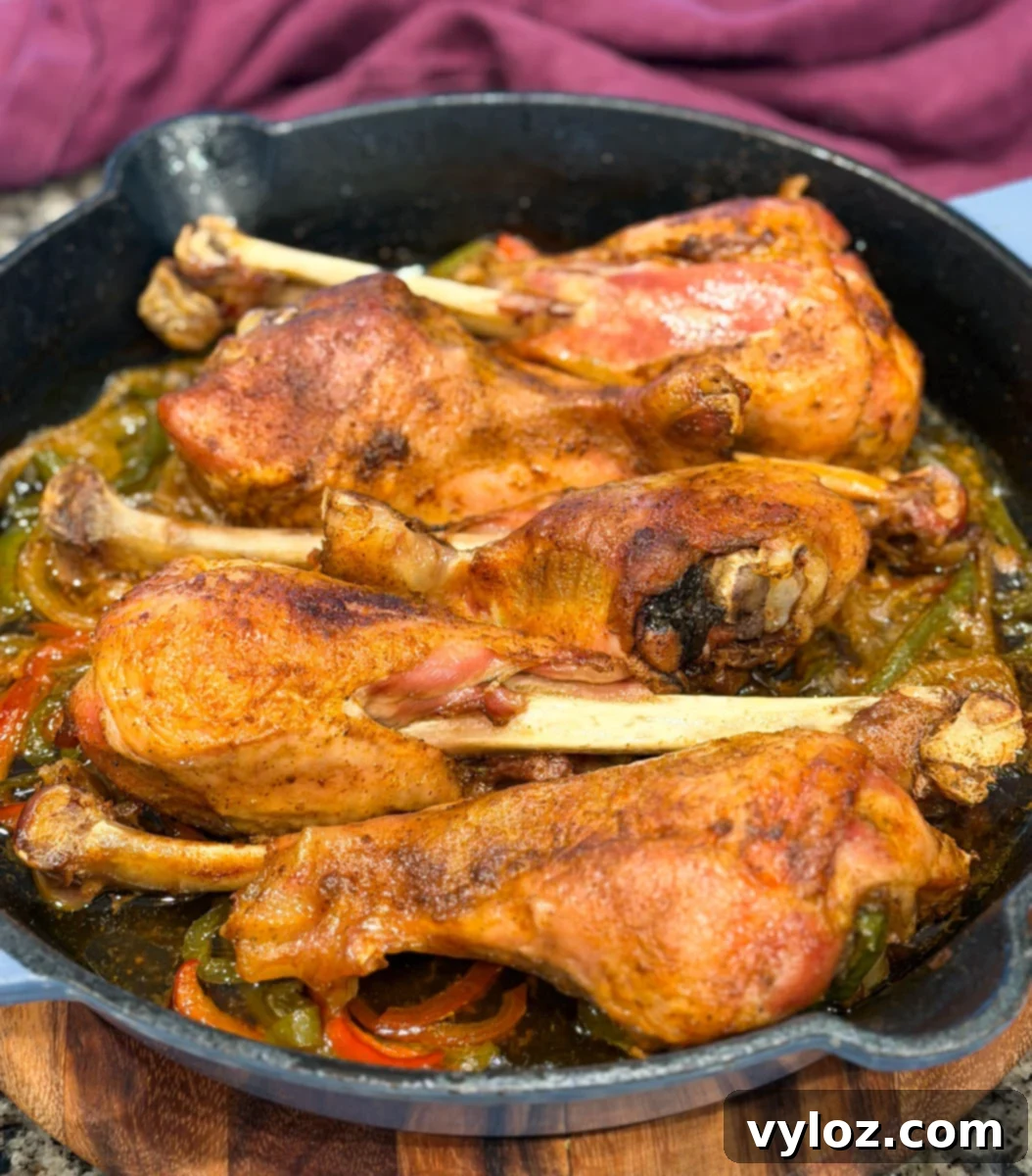 Golden brown baked turkey legs resting in a cast iron skillet with peppers and onions underneath. The turkey skin looks crisp and well-seasoned, with steam rising and juices bubbling at the bottom of the pan.