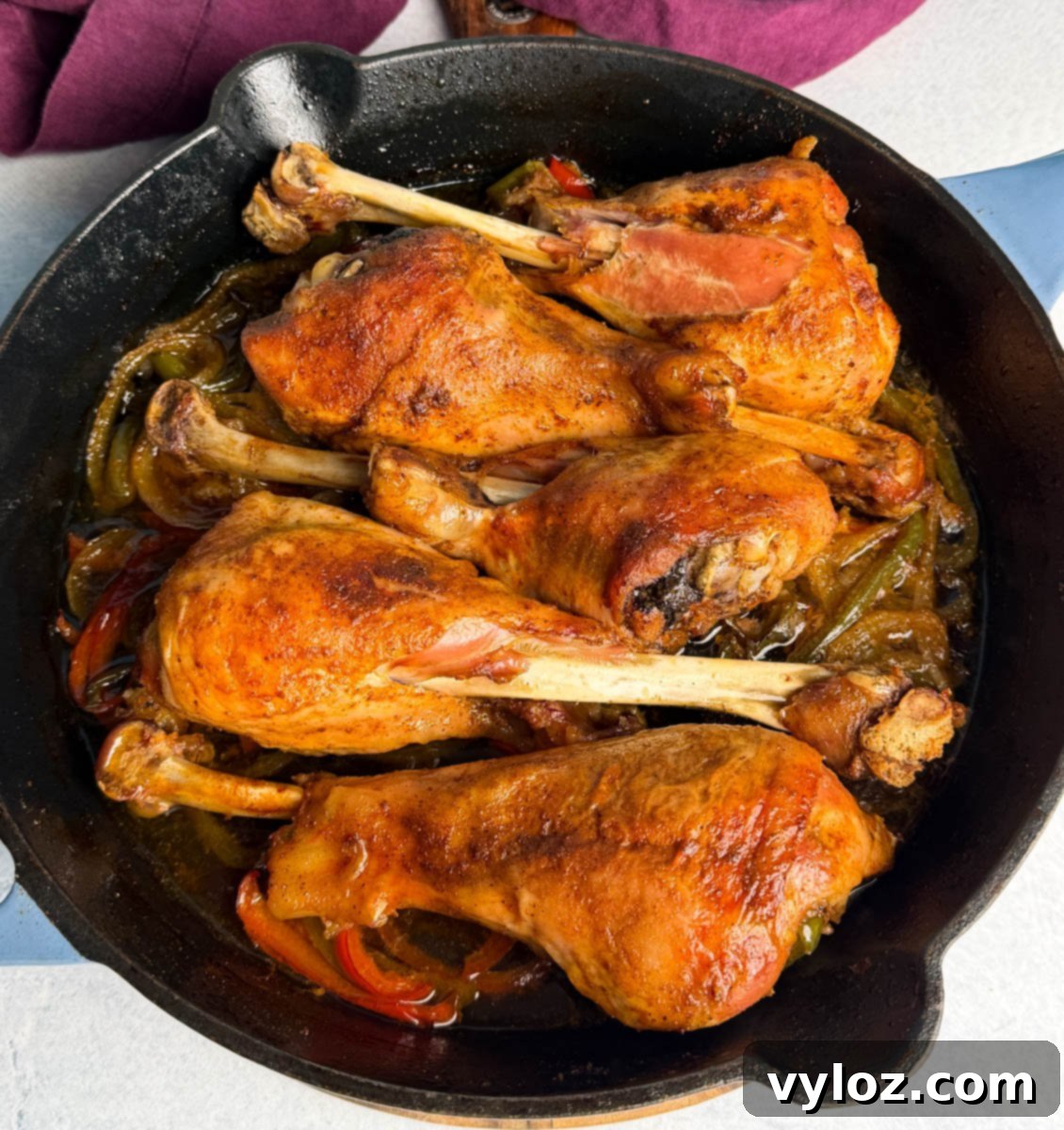 Golden brown baked turkey legs in a cast iron skillet with sautéed onions and bell peppers. The turkey skin looks crisp and caramelized, with rich juices pooling at the bottom of the pan.