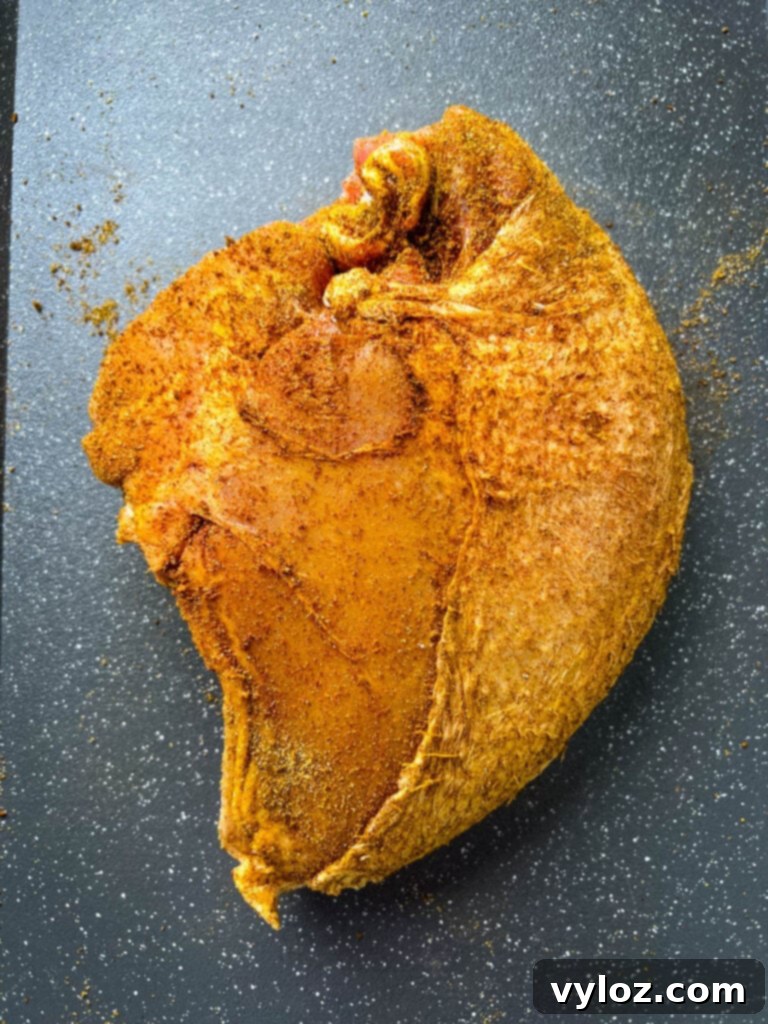 Raw bone-in turkey breast, generously coated with a savory seasoning rub, resting on a sheet pan, ready for slow cooking