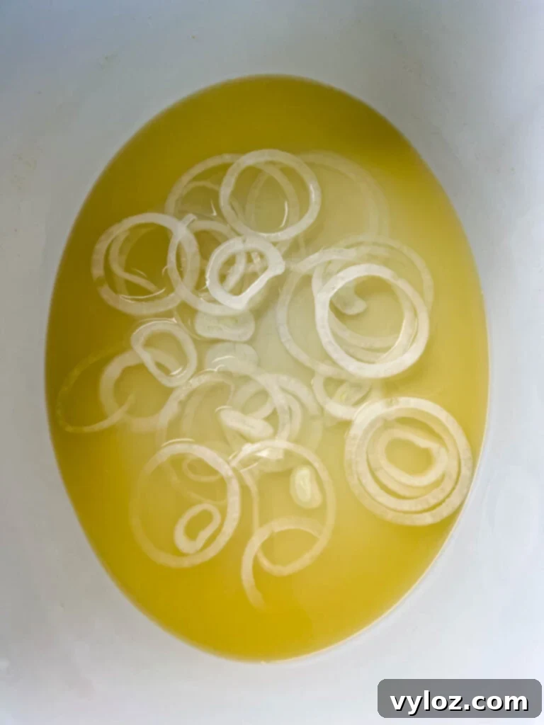 A foundation of vibrant sliced onions and savory broth simmering gently at the bottom of a Crockpot slow cooker