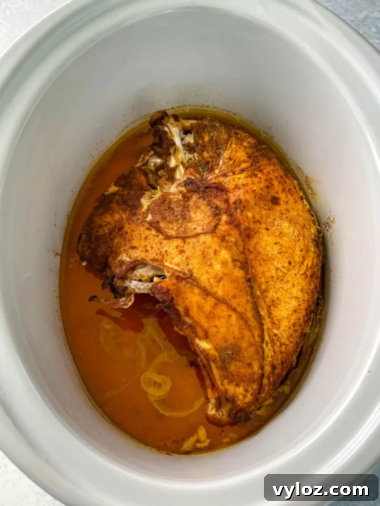 Perfectly cooked bone-in turkey breast, glistening and tender, ready to be carved directly from the Crockpot slow cooker
