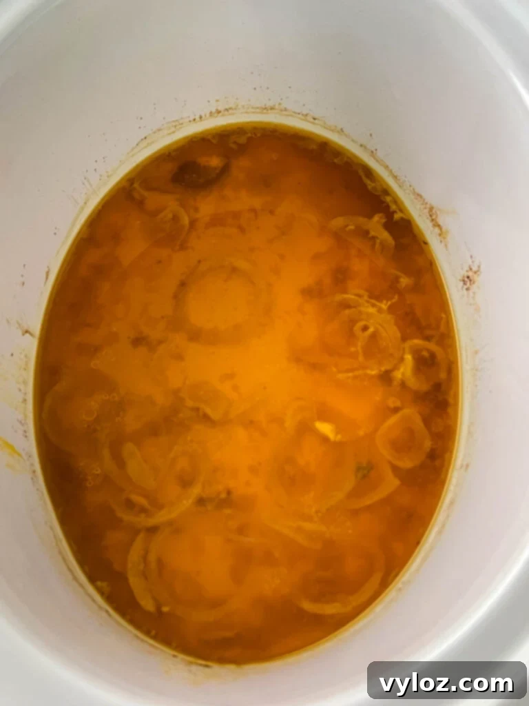 A slow cooker pot with rich turkey drippings collected at the bottom