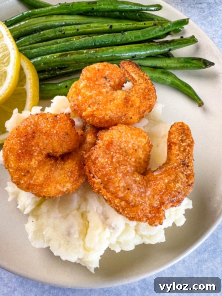 Mouthwatering Lemon Pepper Shrimp, expertly seasoned and served alongside creamy mashed potatoes and vibrant green beans on a white plate, garnished with fresh herbs and lemon wedges.
