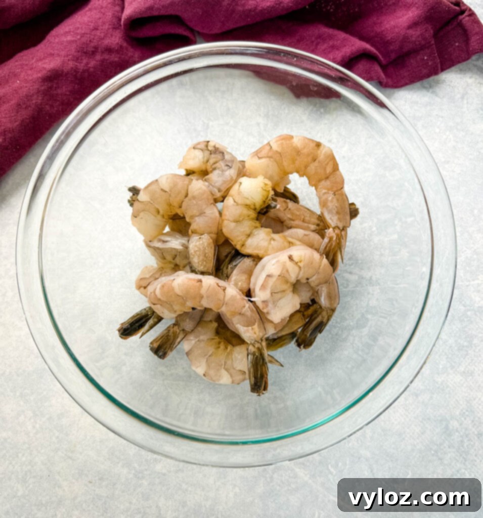 A glass bowl filled with fresh, raw, peeled, and deveined shrimp, ready to be seasoned and cooked.
