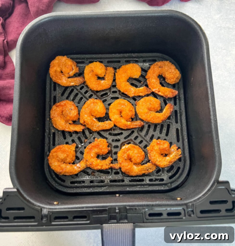 Lemon pepper shrimp cooking to perfection in an air fryer basket, showing a vibrant pink color.