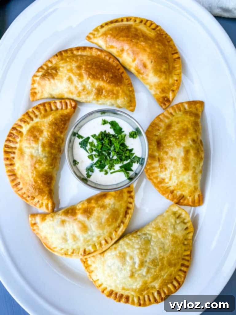 A stack of perfectly golden beef and cheese empanadas on a white plate, ready to be enjoyed.