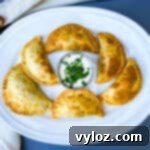 Golden-brown beef empanadas served on a white plate with a side of creamy white sauce and fresh cilantro garnish