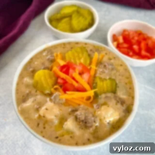 Hearty Slow Cooker Cheeseburger & Potato Soup 12 slow cooker cheeseburger soup in a white bowl with shredded cheese, pickles, and tomatoes