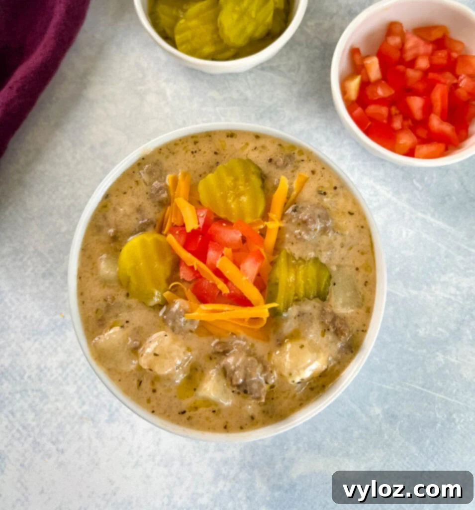 Hearty Slow Cooker Cheeseburger & Potato Soup 10 slow cooker cheeseburger soup in a white bowl with shredded cheese, pickles, and tomatoes