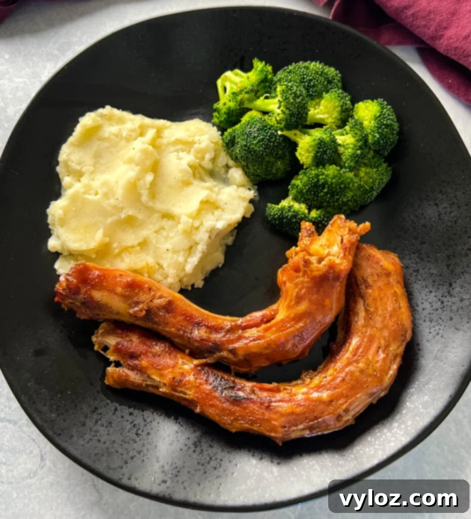 A black plate showcasing beautifully smoked turkey necks, accompanied by creamy mashed potatoes and fresh, steamed broccoli.