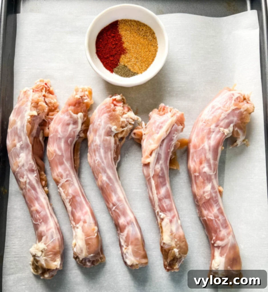 A selection of raw turkey necks sits on parchment paper, surrounded by a vibrant bowl of aromatic spices ready for seasoning.