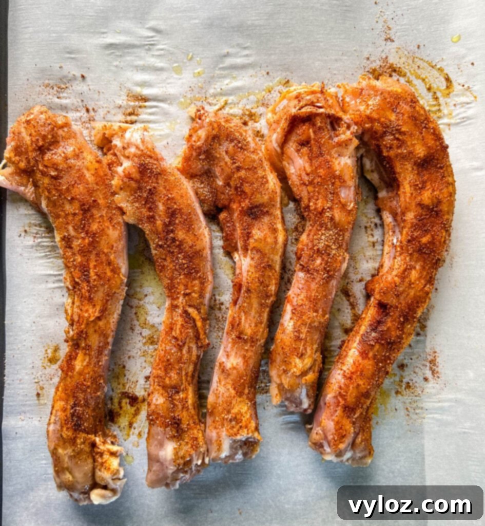 Raw turkey necks, generously coated with a rich blend of Creole seasoning, smoked paprika, salt, and pepper, are arranged on parchment paper, ready for the smoker.