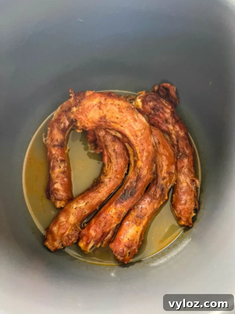 Fully smoked and tender turkey necks are shown inside a pressure cooker, having completed their braising stage for ultimate tenderness.