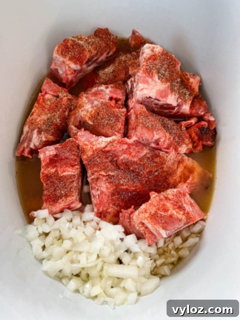 Raw pork neck bones, sliced onions, and broth arranged in a Crockpot slow cooker, ready for cooking