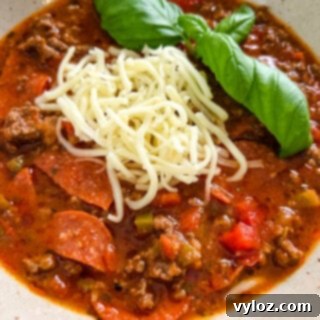 Hearty pizza soup with ground beef, vibrant pepperoni slices, melted mozzarella, and fresh basil in a rustic bowl