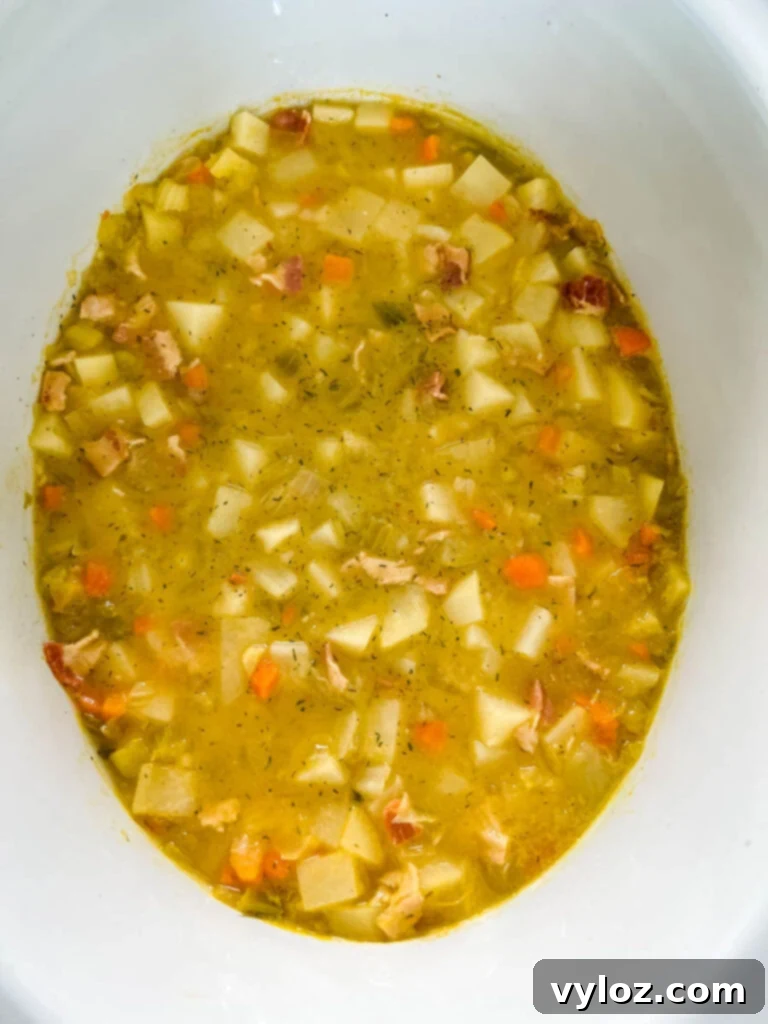 Ultimate Slow Cooker Loaded Potato and Bacon Soup 7 Creamy loaded potato soup, rich and inviting, cooking in a Crockpot slow cooker, promising a delicious meal.