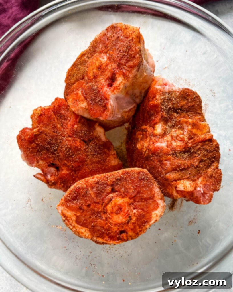 Raw oxtail pieces, generously coated with a savory seasoning blend, resting in a glass bowl, ready for cooking