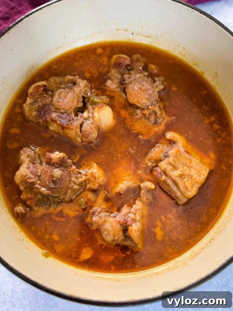 Close-up of tender, slow-cooked oxtail pieces submerged in a rich, savory broth in a pot, ready for serving or gravy preparation