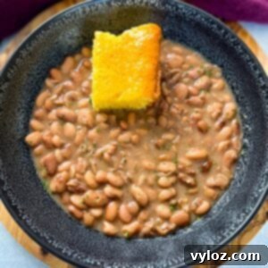 A black bowl filled with savory pinto beans, succulent ham hocks, and a golden slice of cornbread