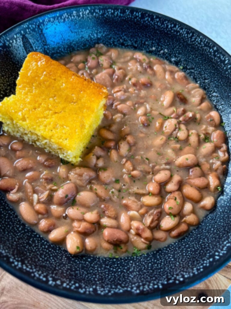 A full black bowl featuring pinto beans, ham hocks, and cornbread, highlighting its hearty appeal