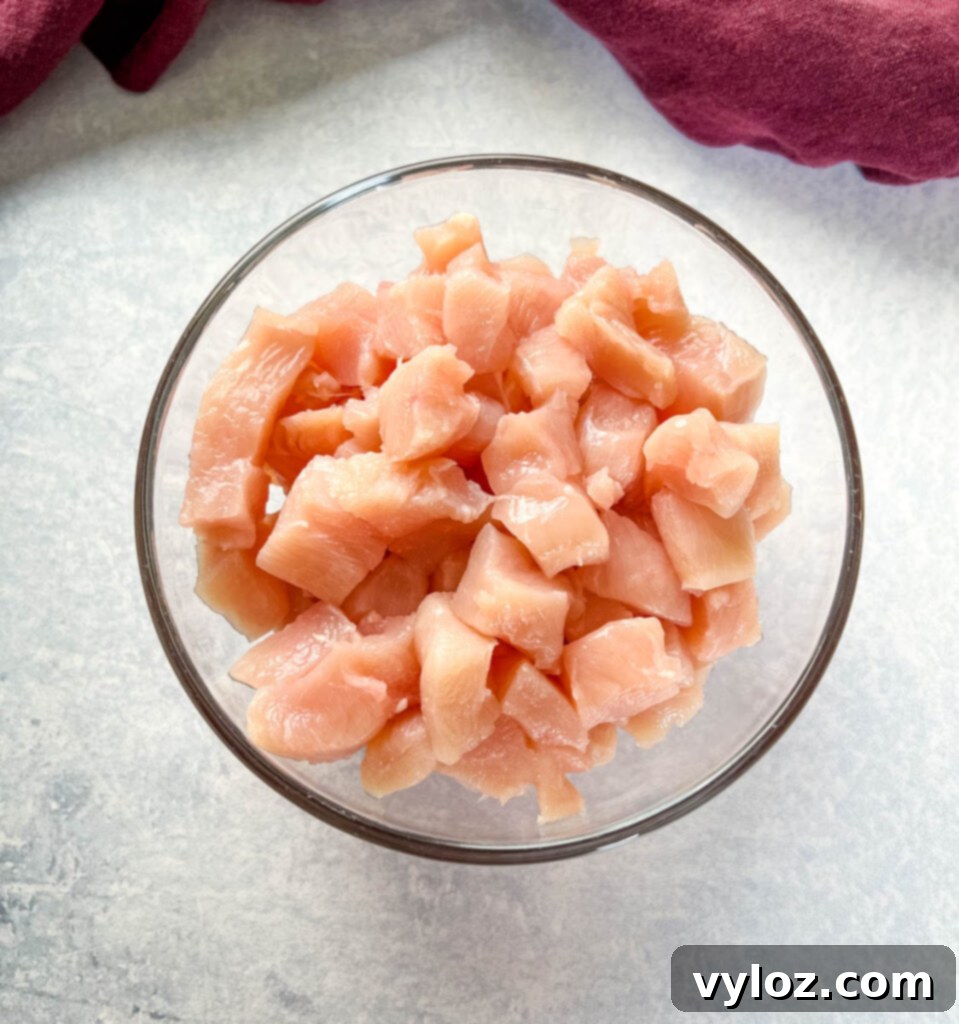 Raw chicken breasts, sliced into small, uniform pieces, in a clear glass bowl.