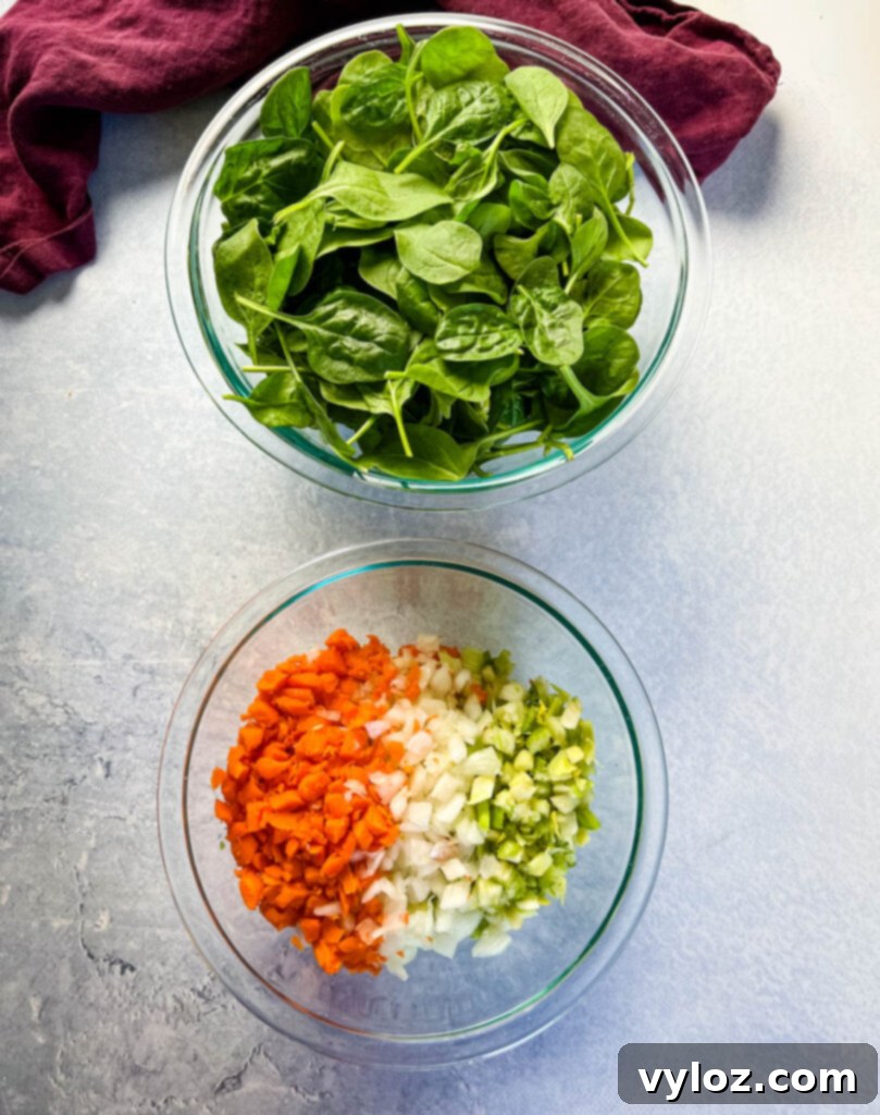 Separate bowls displaying fresh spinach, sliced carrots, chopped celery, and diced onions, ready for cooking.