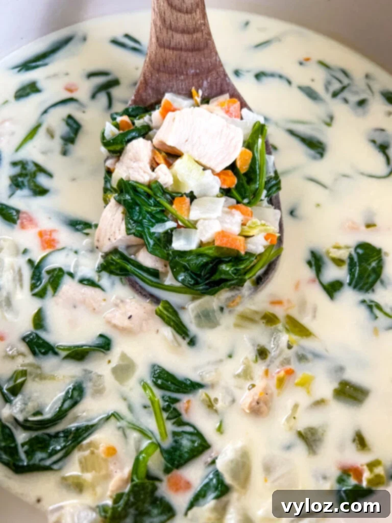 A wooden spoon stirring Creamy Chicken Florentine Soup in a pot, highlighting the creamy texture and spinach.