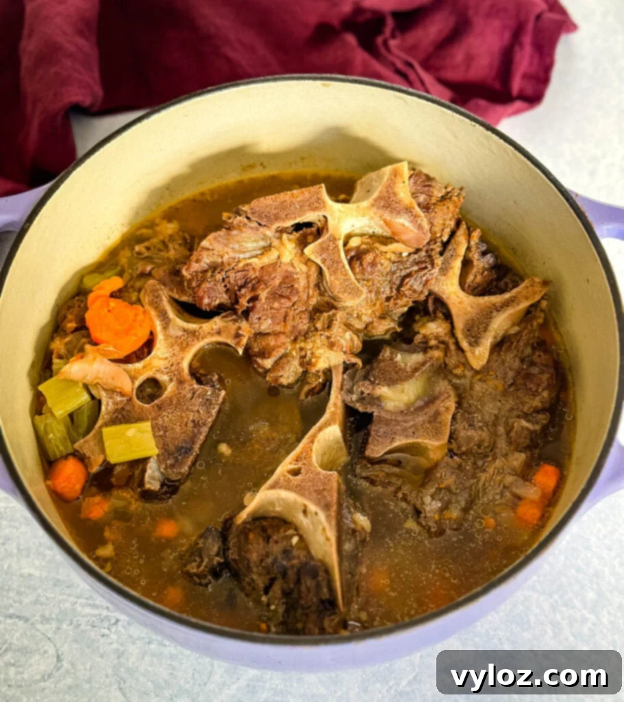 Close-up of beef neck bones simmering in a pot with vegetables, showing the tender meat