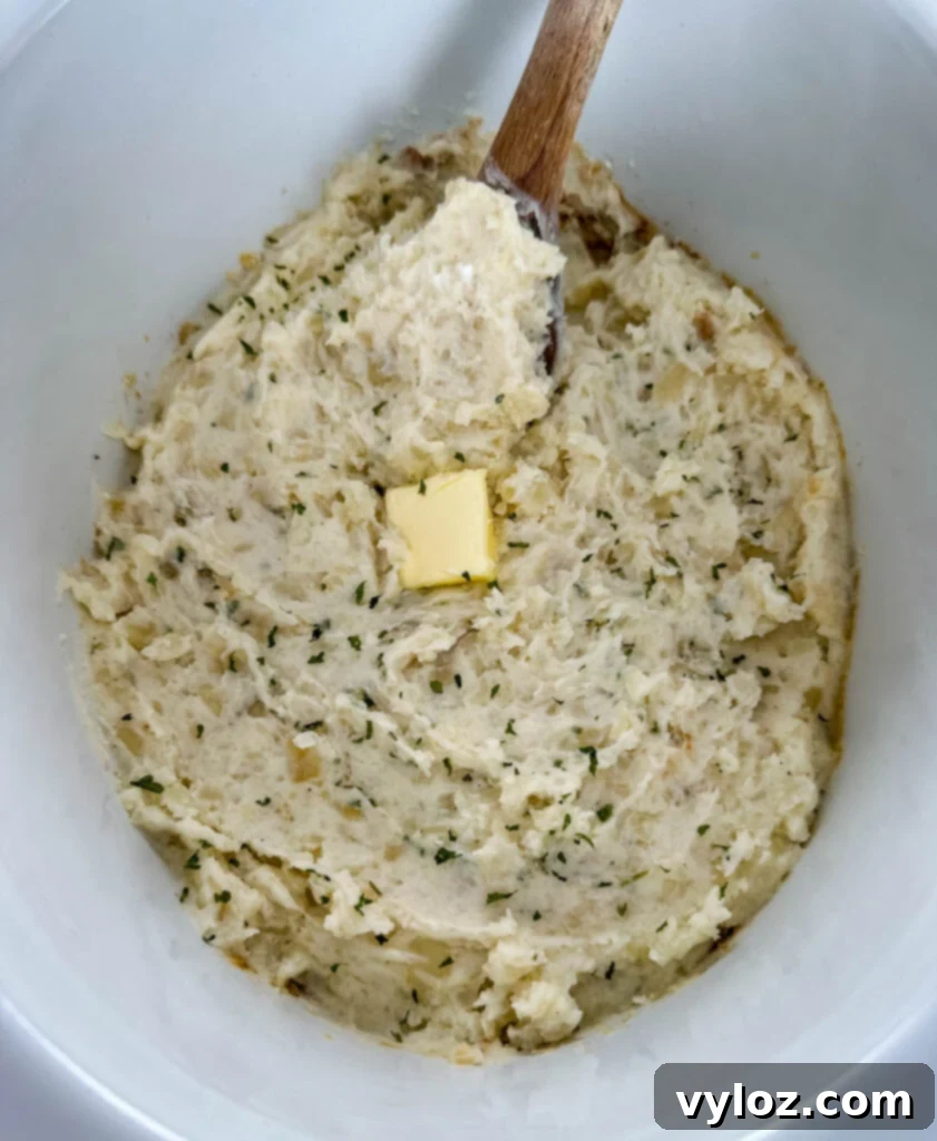 Close-up of perfectly mashed potatoes in a Crockpot slow cooker, with a pat of butter melting on top, indicating readiness.