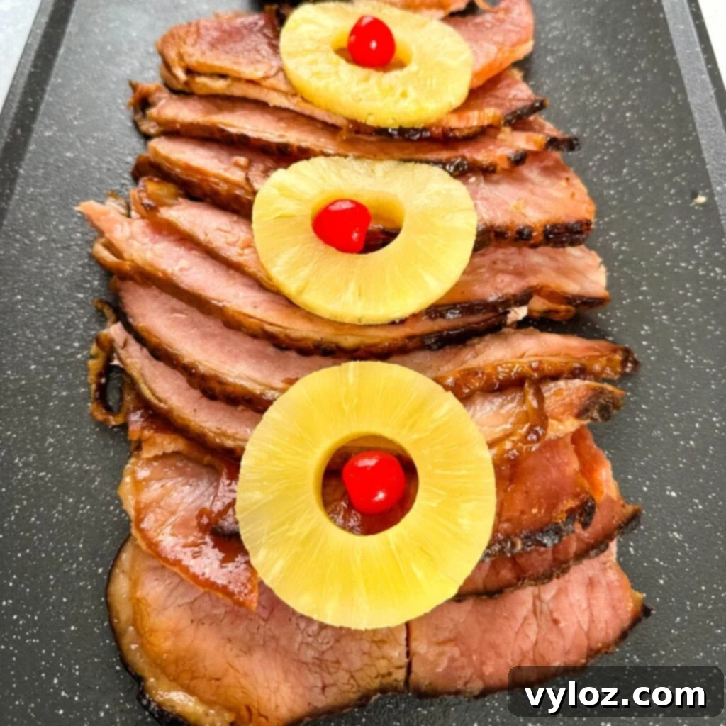 Serving of slow cooker Crockpot ham on a plate, garnished with pineapple slices and a generous pour of glaze
