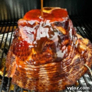 Smoked ham on a Traeger pellet grill brushed with honey brown sugar glaze