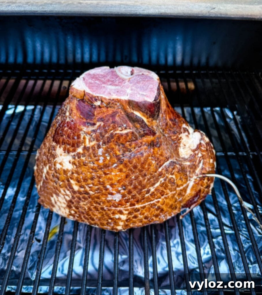 Large bone-in ham resting on a Traeger pellet grill grate, infusing with smoke flavor