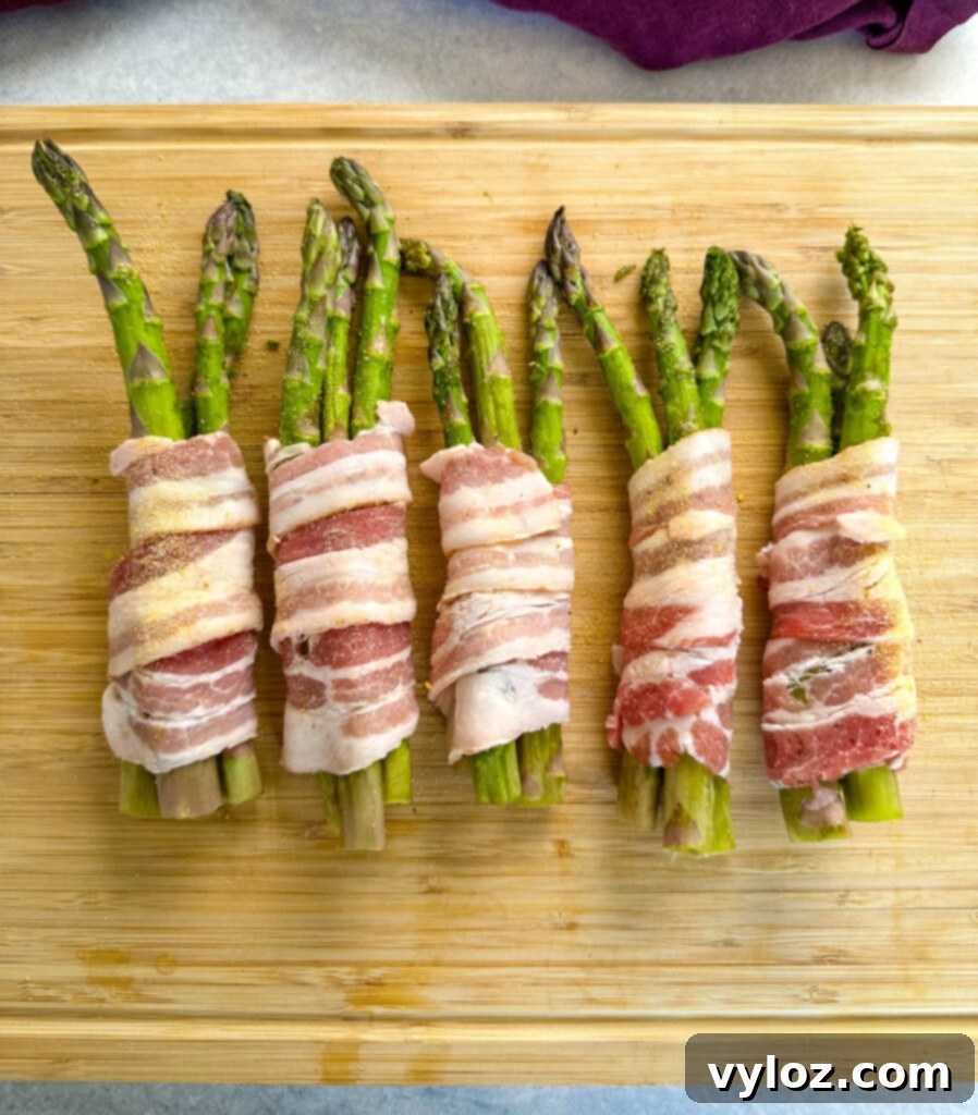 Bundles of bacon-wrapped asparagus on a wooden cutting board, ready for the air fryer